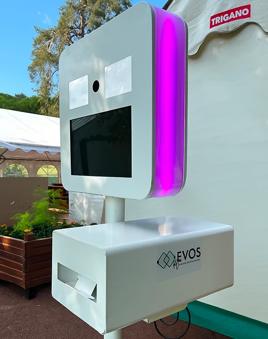 Borne photo EVOS blanche avec écran, flash LED violet et imprimante installée en extérieur sous un barnum